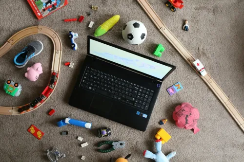 An open laptop on a floor where lots of children&#039;s toys are scattered.