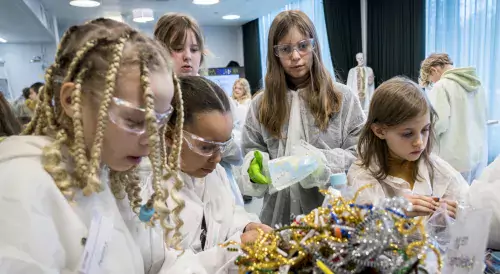 A group of children stand around a table and create fantasy molecules.