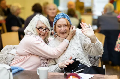 Two women friends smiling together, sitting at a coffee table enjoying themselves.