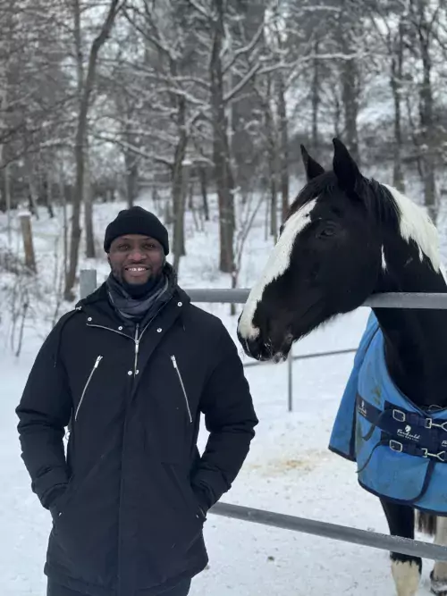 Sergio Nhassengo dressed in black clothes outisde with snow on the ground next to a horse.