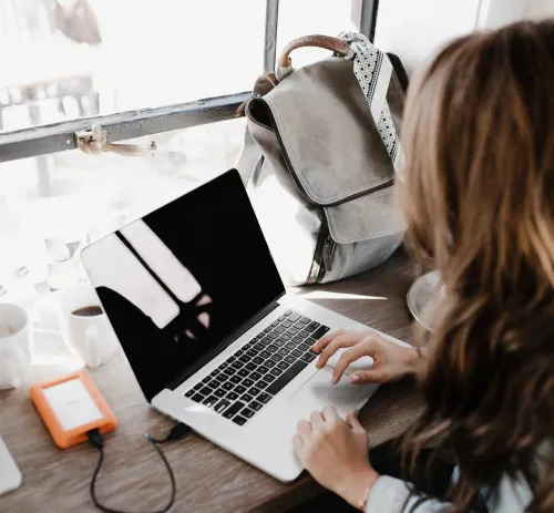 A woman sits with her back to the camera in front of a laptop.