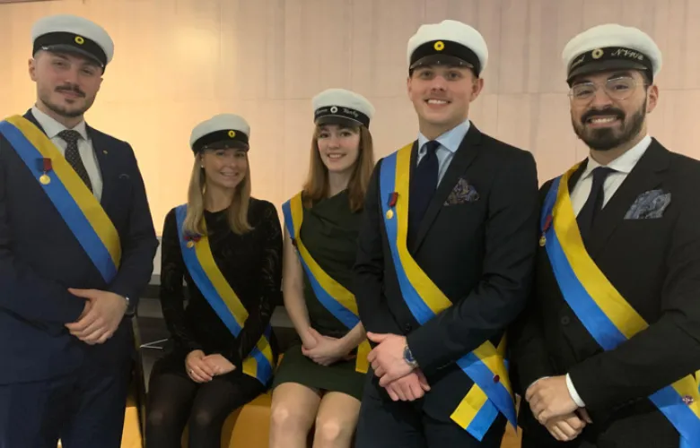Five student ushers dressed in formal wear and Swedish graduation caps.