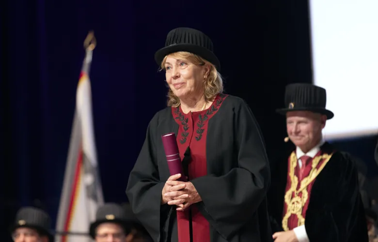 Woman in doctoral hat holding in a diploma.