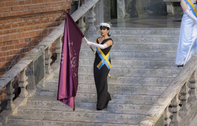 Student marshal walking down the marble stairs in the Blue Hall, carrying KI:s flag.