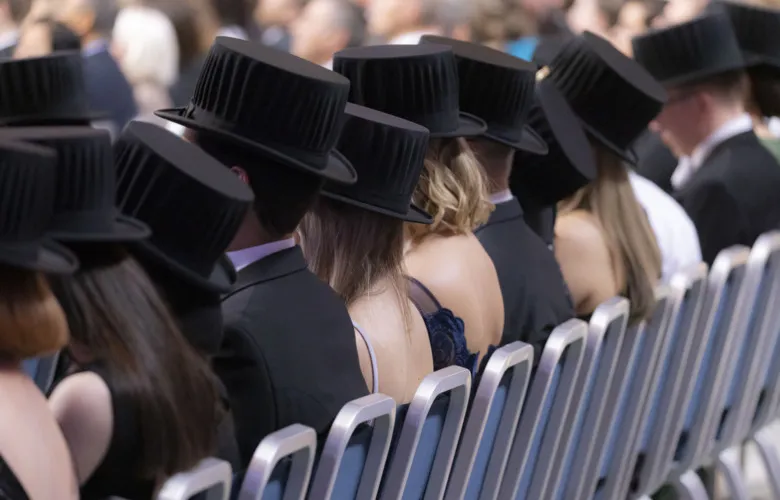 PhD&#039;s with their doctoral hats on sits in a row with their backs against the camera.
